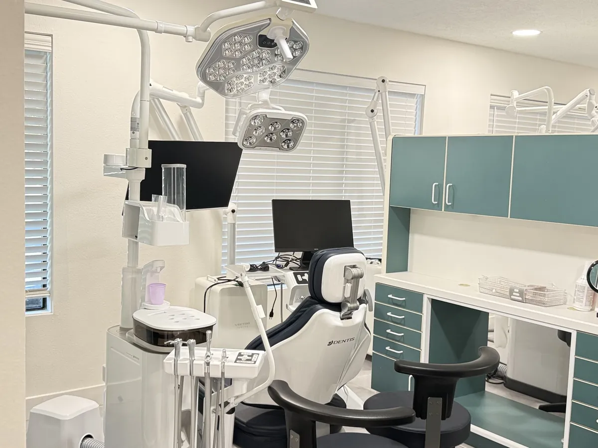 Treatment room with a modern dental chair, overhead lights and teal cabinets at Aloha Dental Specialty Center in Beaverton