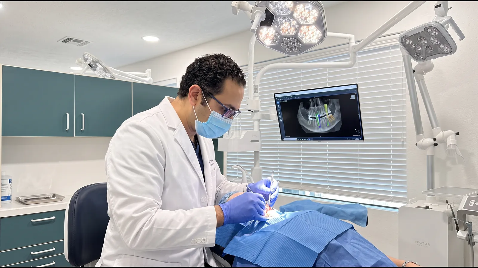 Dr. Walied Eldomiaty treating a patient with a 3D CBCT implant plan displayed on the monitor beside the chair